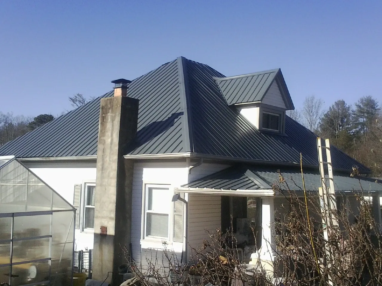 Dark blue standing seam metal roof on a white farmhouse with dormer — Slate & Tile Roof Repair by Roofing Brothers in New Auburn