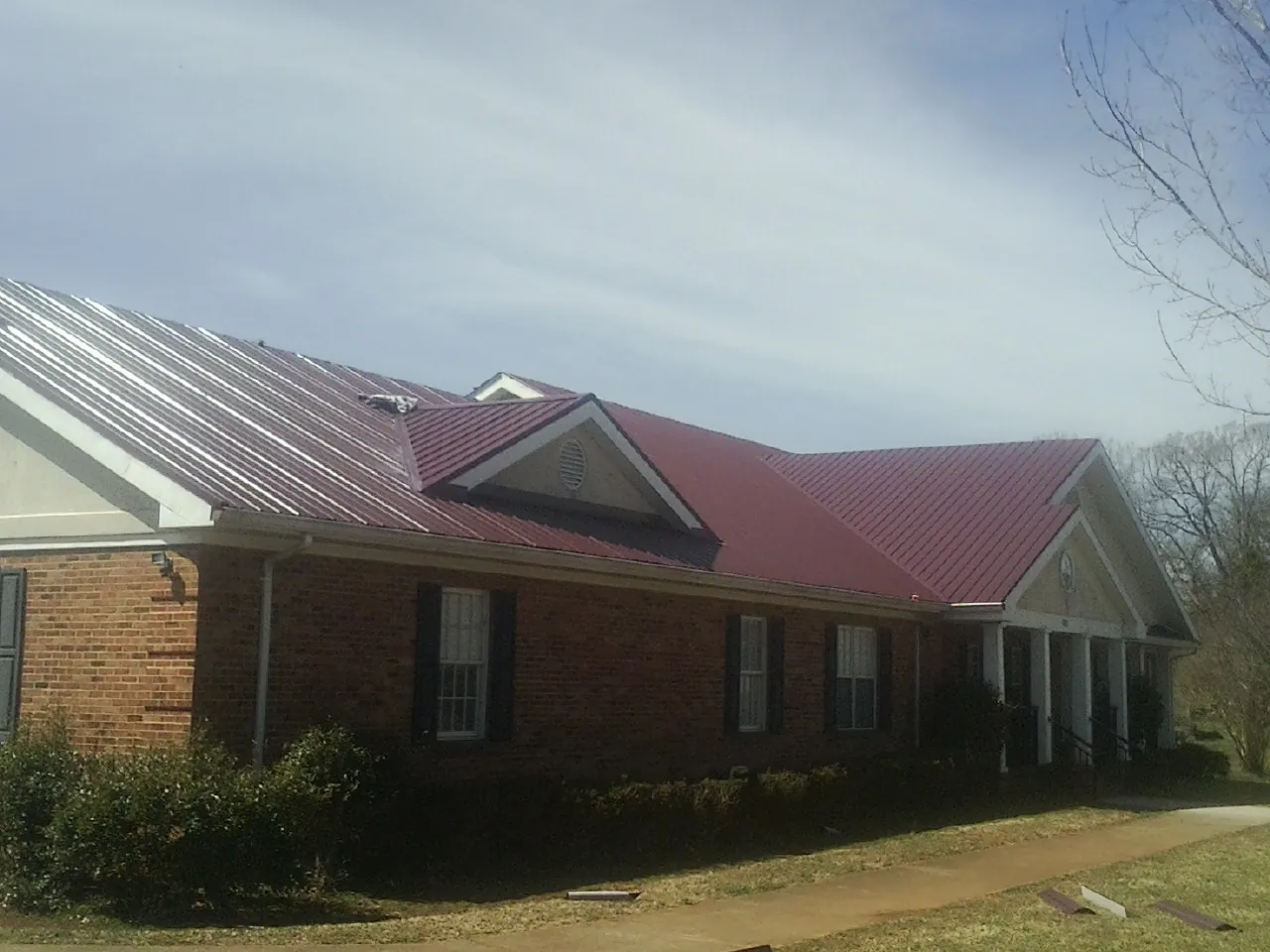 Red metal roof with gabled entries on a long brick building, from a Hail Damage Roof Repair job in New Auburn