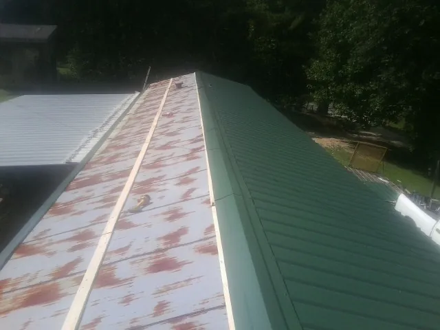 Old rusted panels beside newly installed green metal roofing — Wind Damage Roof Repair by Roofing Brothers in New Auburn