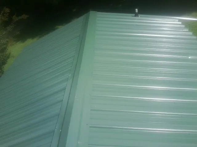 New green metal panels meeting at the ridge of a roof — Flat Roof Repair work by our crew in New Auburn