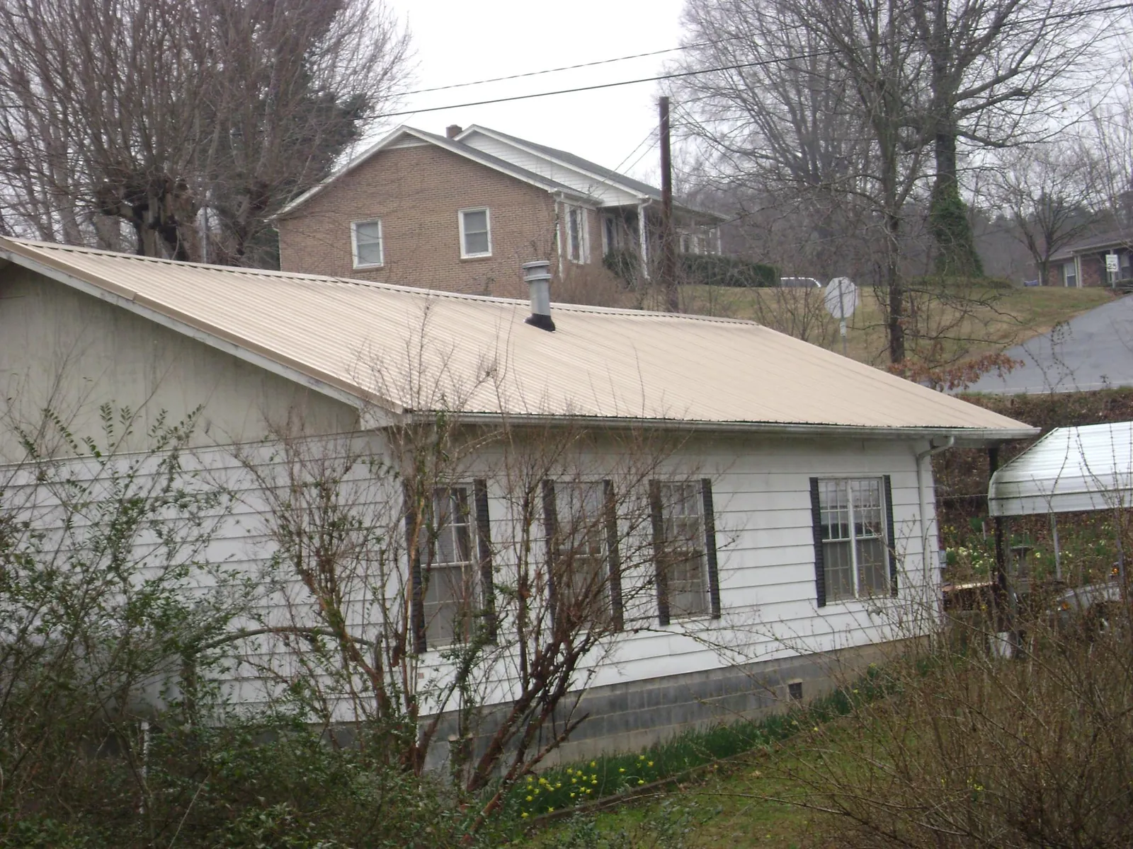 Tan metal roof on a white sided house set into a hillside — Commercial Roofing by Roofing Brothers in New Auburn