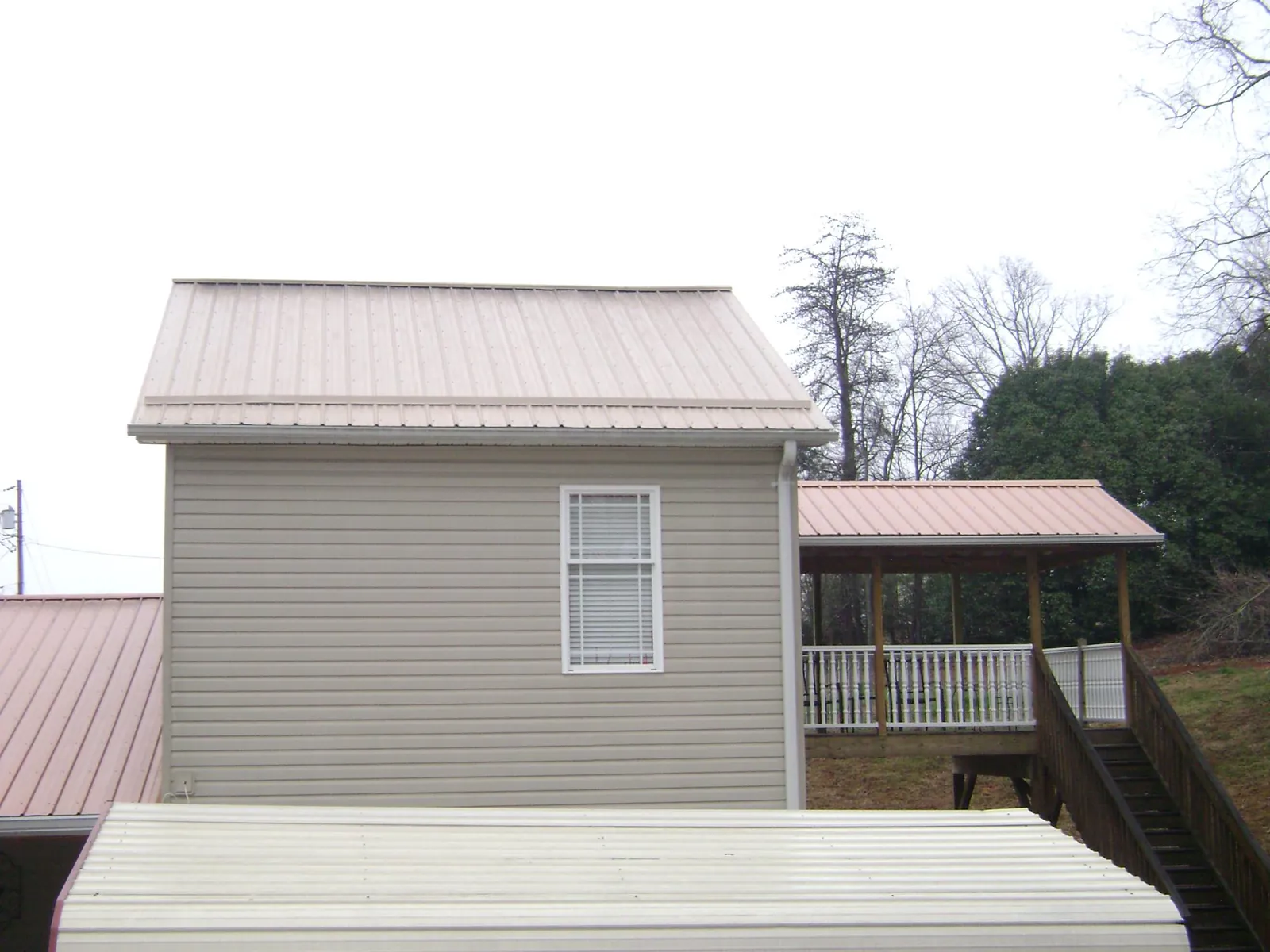 Tan metal roofs on a two story addition and attached porch, from a Roof Replacement job in New Auburn